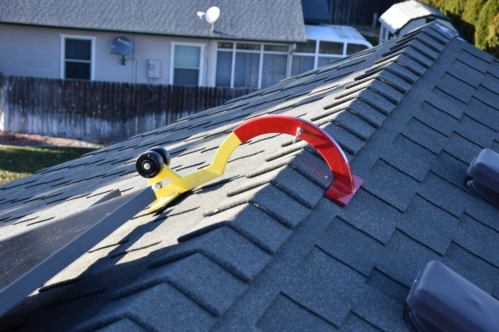 A non-penetrating safety anchor resting over the peak of a shingle roof
